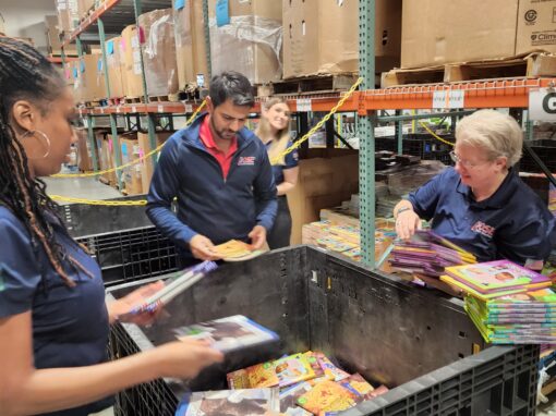 Three people sort and organize children's books in a warehouse for a Chicagoland literacy partnership, placing them into large bins. Shelves and boxes are visible in the background.