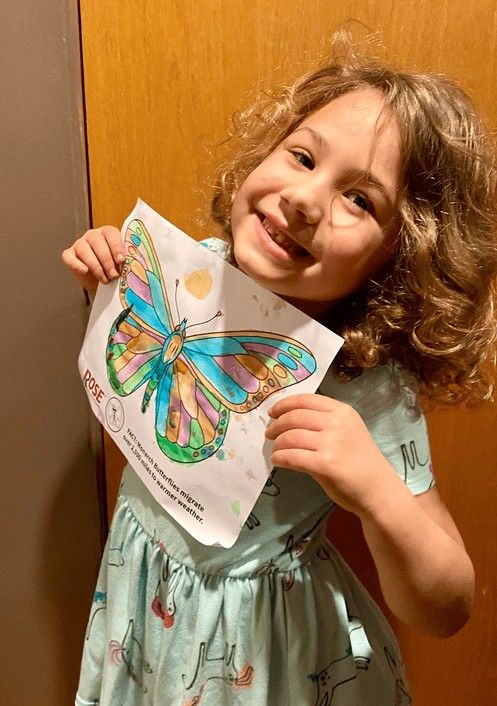 Rose Colorin Child holding a colorful butterfly drawing from an art activity indoors