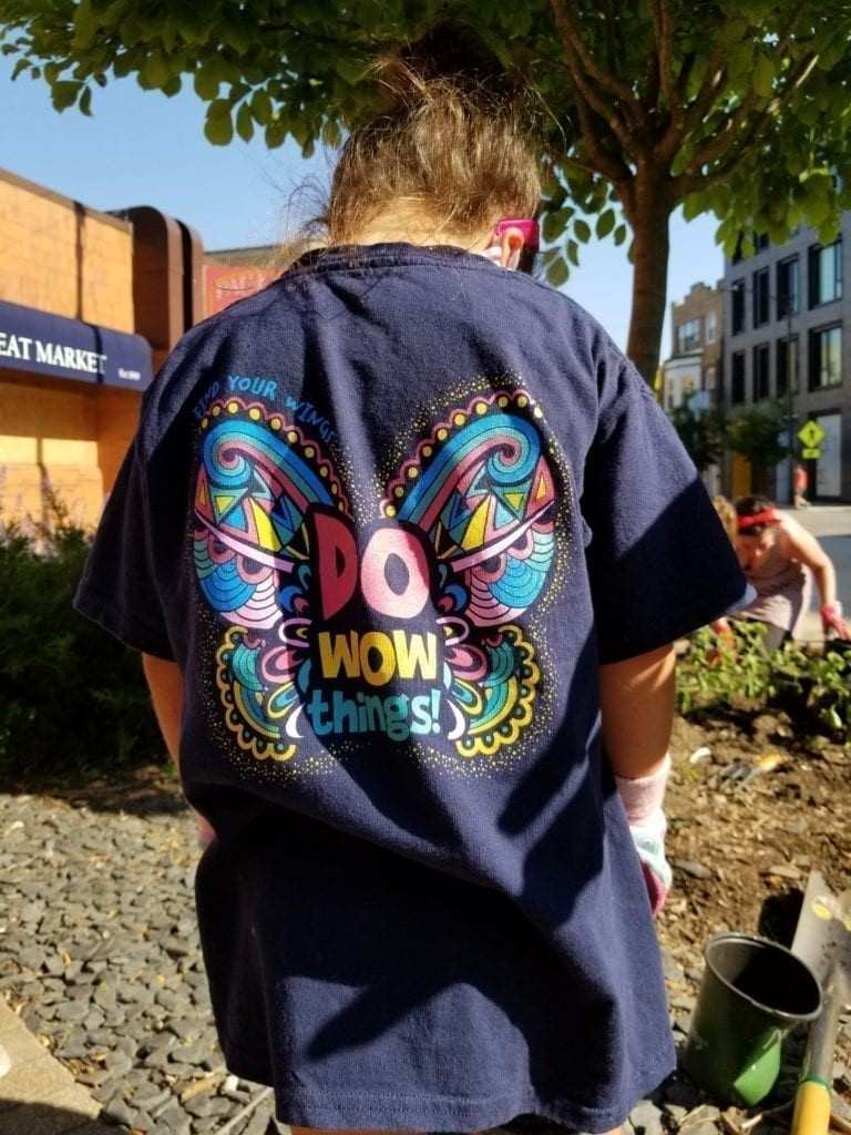 Person wearing a colorful “Do WOW Things!” shirt while gardening outdoors