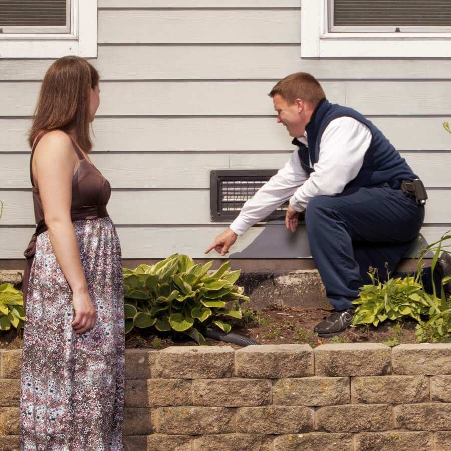 Home inspector points to an exterior foundation area while speaking with a homeowner<br />
