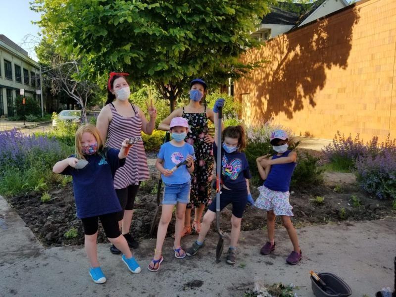 Group of masked volunteers and children posing with gardening tools in a community garden